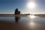 Experience the raw grandeur of Canon Beach, Oregon through this evocative portrayal of dramatic rock monoliths reflecting in the dark, wet sands.