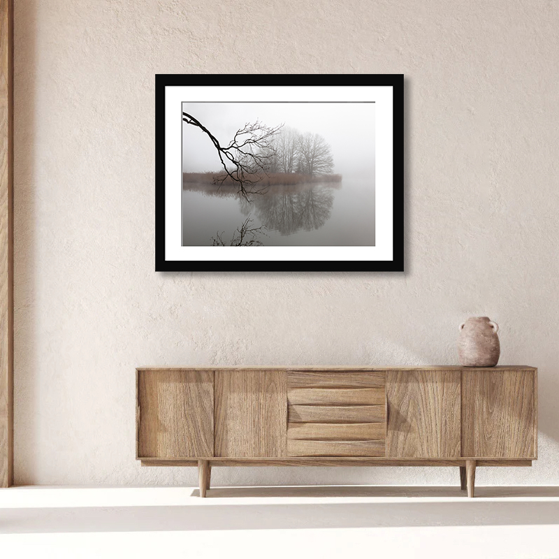 This tranquil image captures a lone island amidst a foggy lake, mirrored by bare fall branches in the Czech Republic.