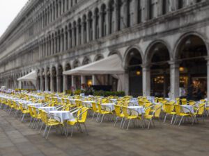 This vibrant piece captures a contrast of spirits, where radiant yellow chairs defy the grey atmosphere at Piazza San Marco,