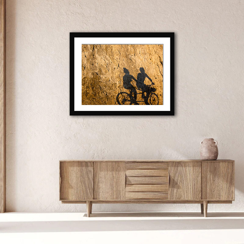 Tranquil synergy of light and shadow, as cyclists cast elongated figures on a sunlit rock wall, epitomizing Vancouver’s vibrant seawall in Stanley Park.