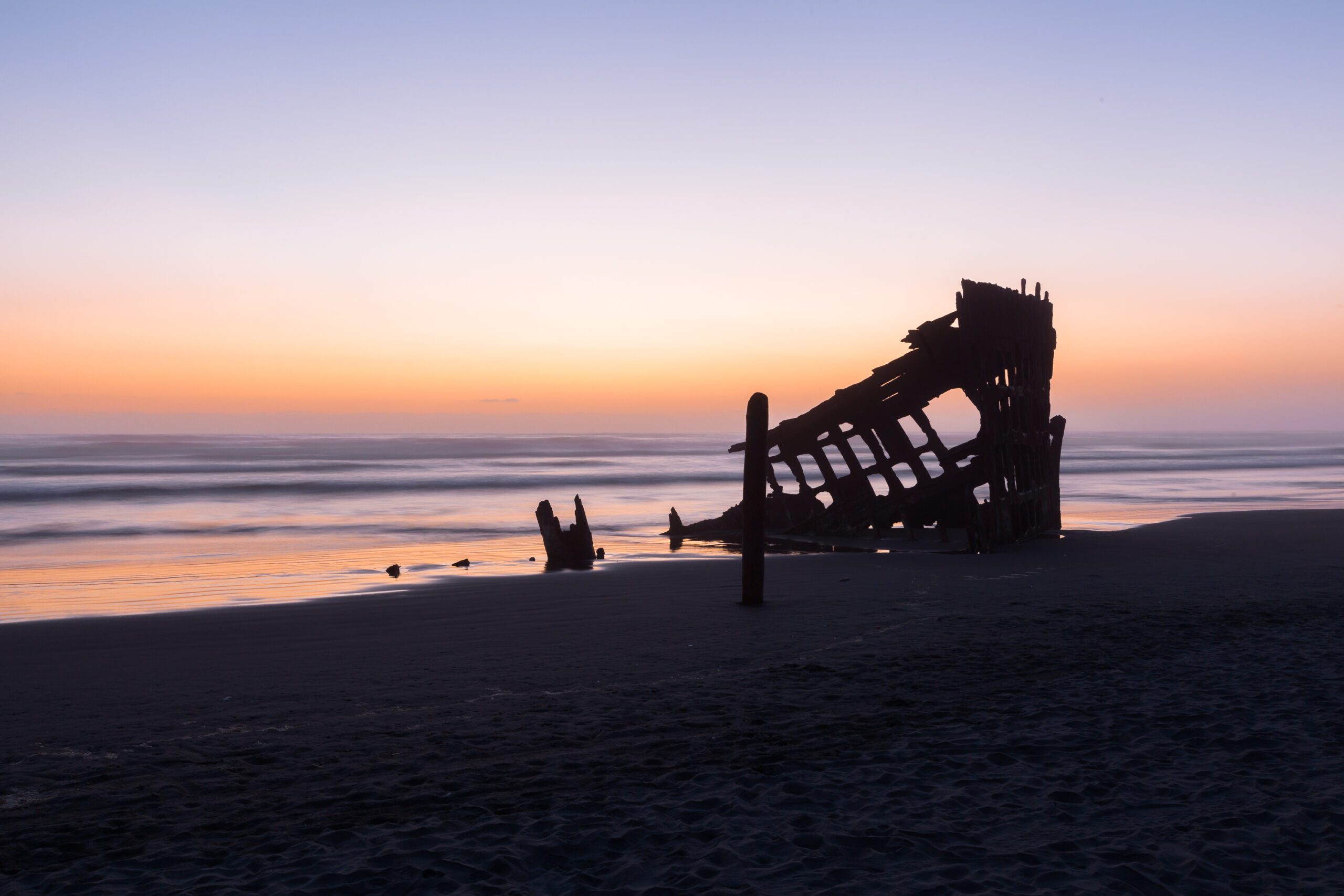 This print encapsulates a haunting yet breathtaking view of the Peter Iredale shipwreck, gloriously silhouetted against a vibrant sunset