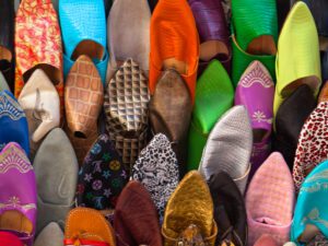 Immerse in the vibrant and bustling life of a Moroccan medina with this arresting image, showcasing a colorful array of shoes on display.