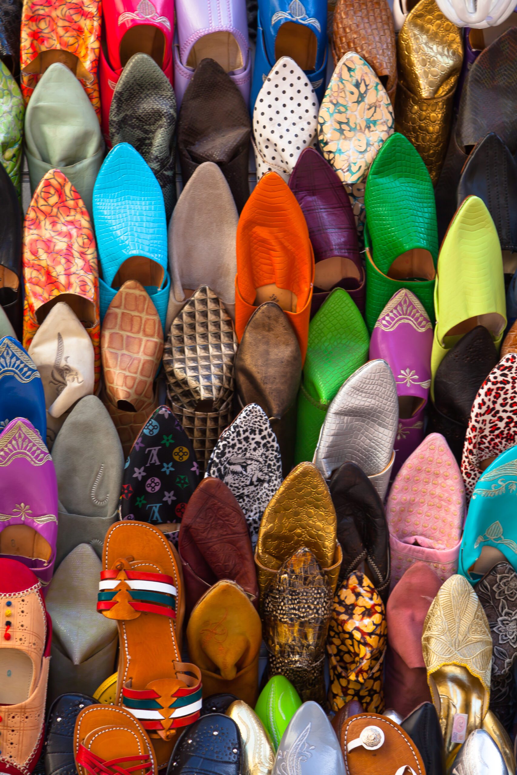 Immerse in the vibrant and bustling life of a Moroccan medina with this arresting image, showcasing a colorful array of shoes on display.