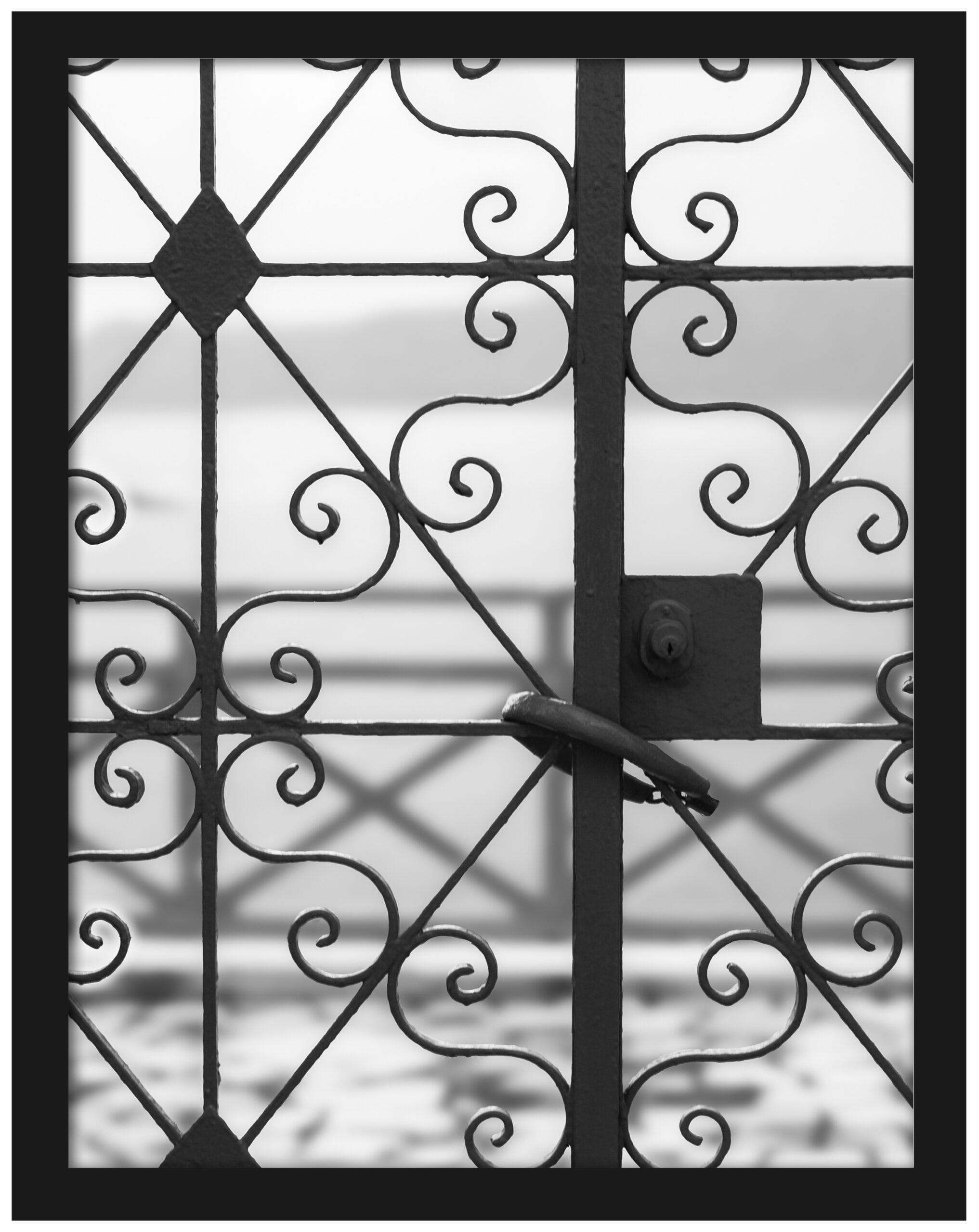 Black and white photo of an old iron gate in Fira, Santorini overlooking the sea.