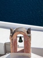 Ancient coral-colored bell against the dark blue ocean in Santorini, Greece.