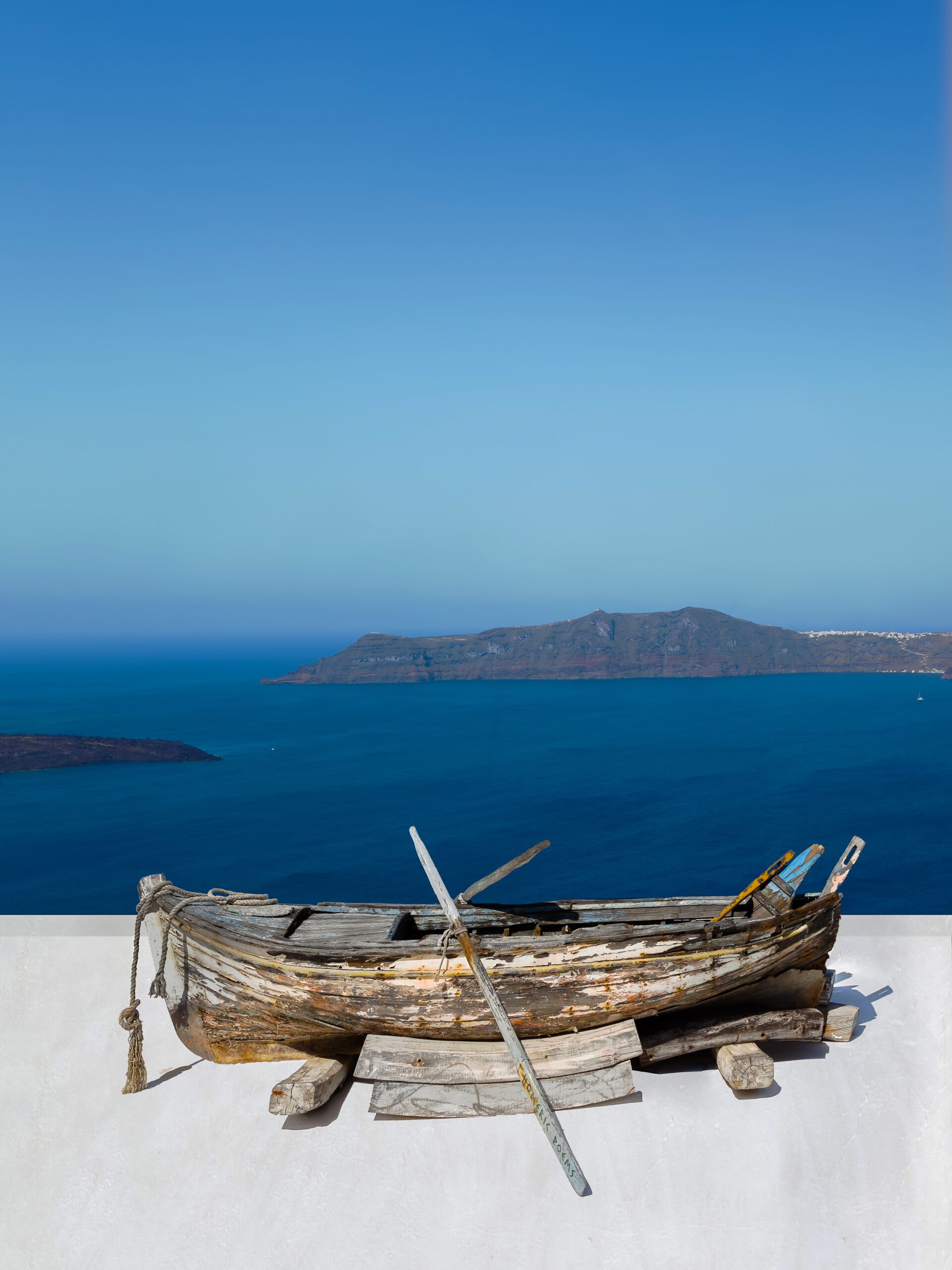 Old rowboat on a white rooftop overlooking the blue caldera in Santorini.