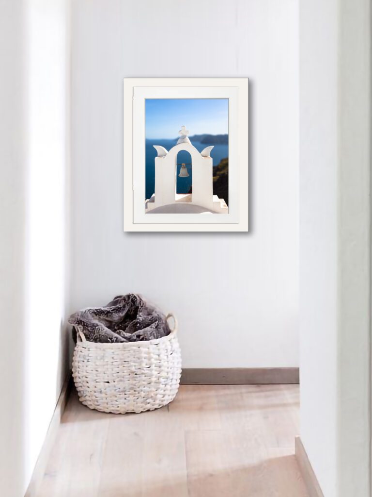 White bell tower with an angel sculpture on top, overlooking the deep blue sea in Santorini, Greece.